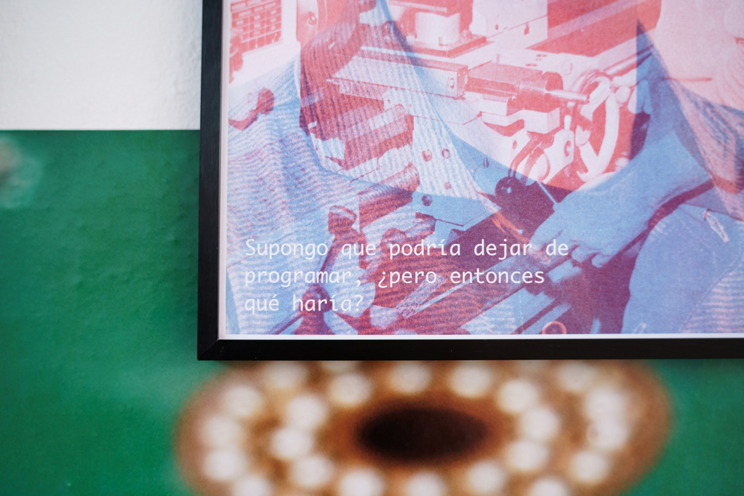 Detail of a risograph poster overlaying a photo of hands operating machinery with Spanish text reading 'Supongo que podría dejar de programar, ¿pero entonces qué haría?'